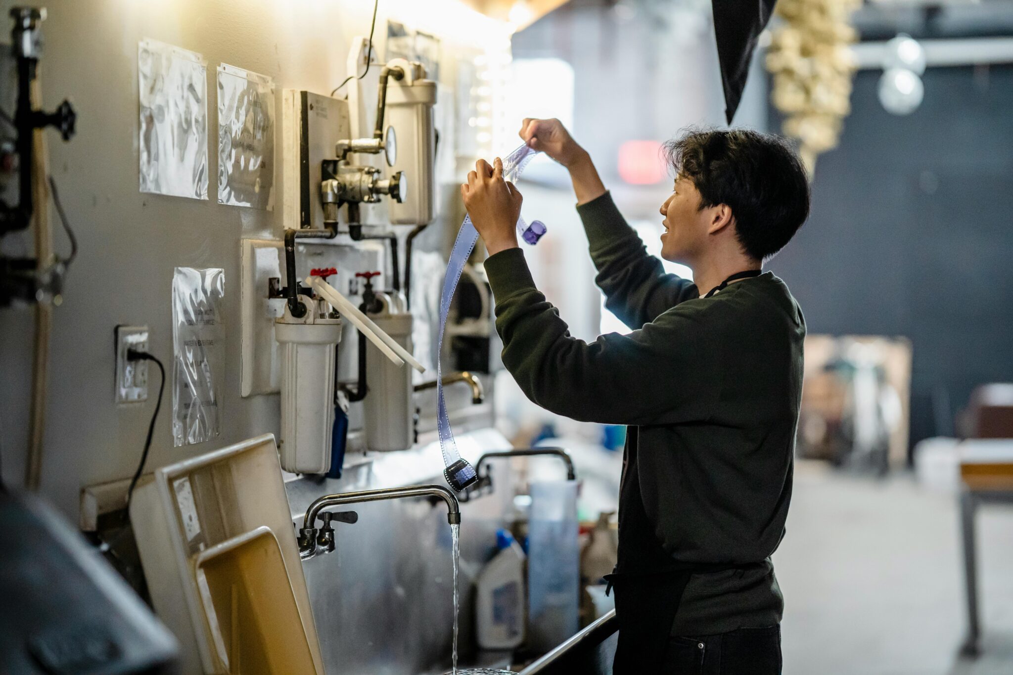 An adult in a darkroom setting develops film, showcasing traditional photography techniques.